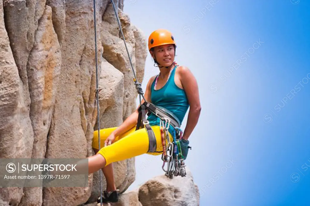 Female rock climber abseiling down cliff face