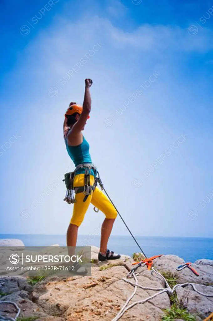 Female rock climber standing on mountain peak with arms up celebrating her success