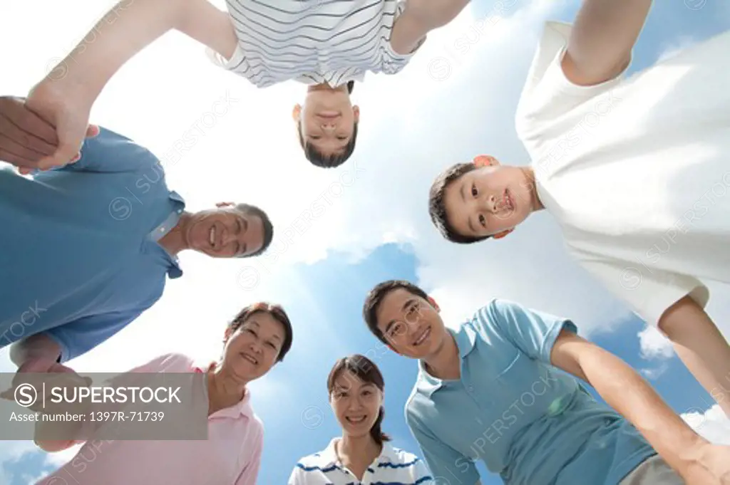 Multi-generational family standing in huddle, holding hands, low angle view