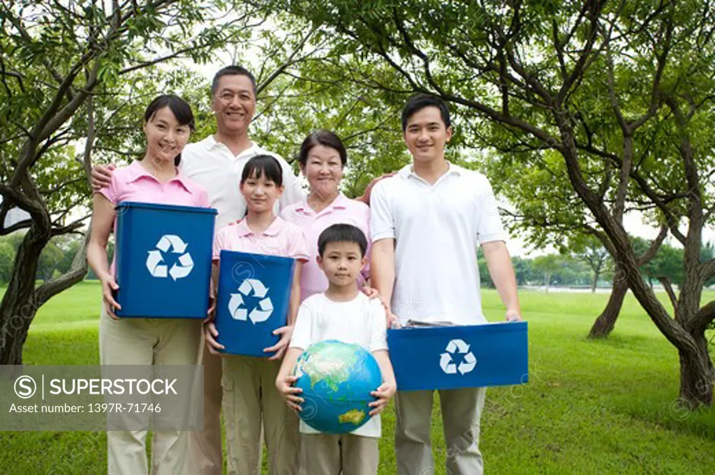 Multi-generational family standing together in a park holding recycling bins and globe in their hands