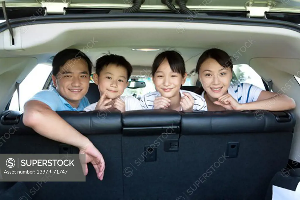 Family sitting in back of car looking out back door, smiling