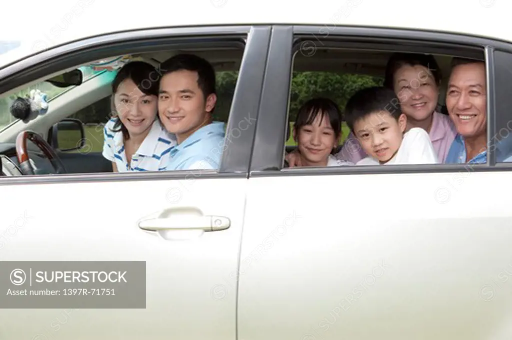 Multi-generational family sitting in car and looking out through car windows, smiling