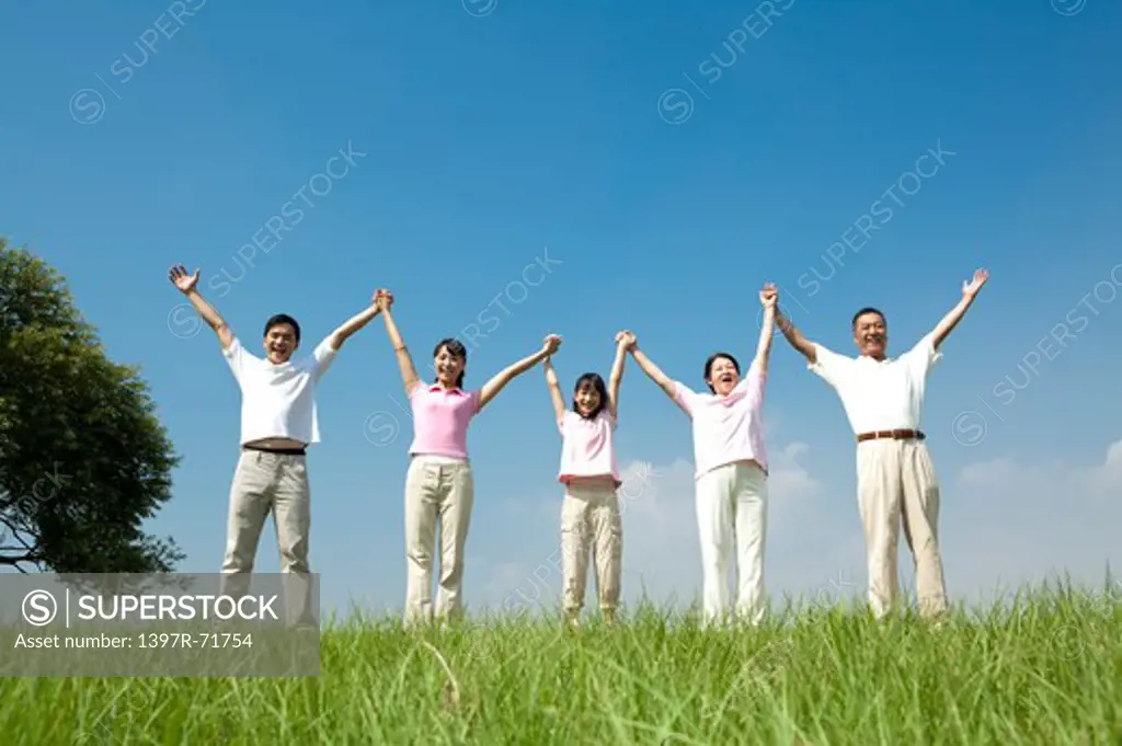Multi-generational family standing in a row on lawn, arms up, holding hands