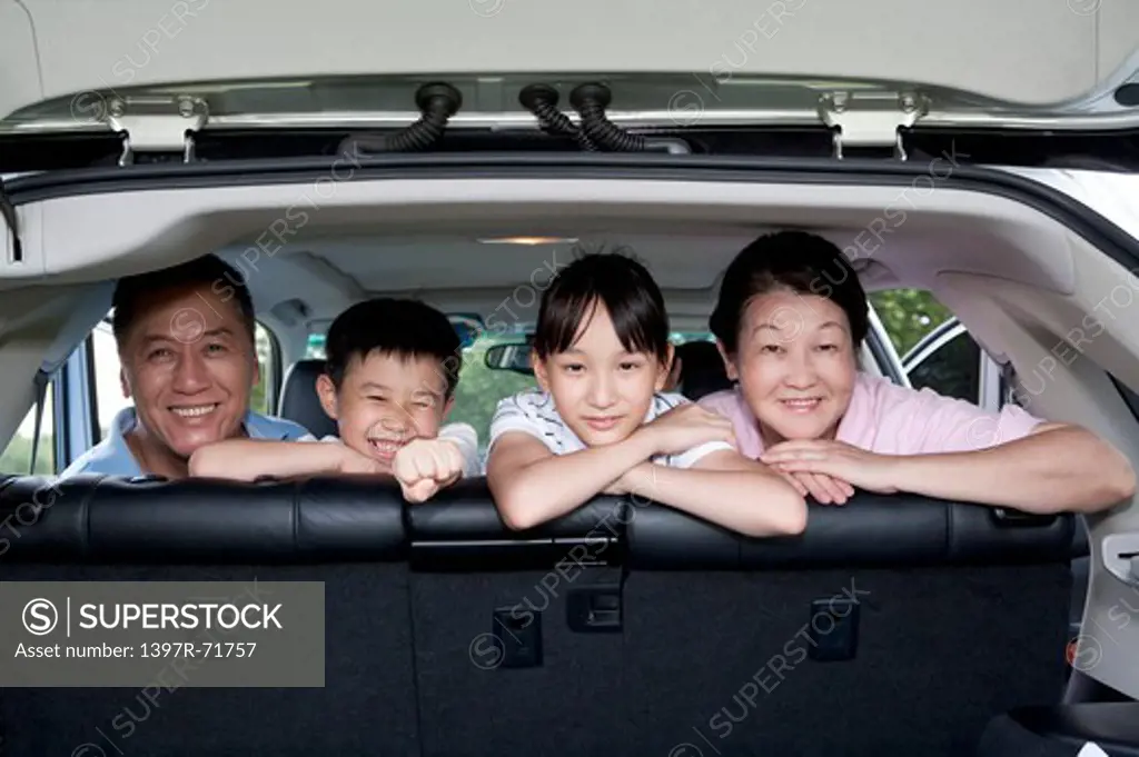 Grandparents and grandchildren sitting in back of car looking out back door, smiling