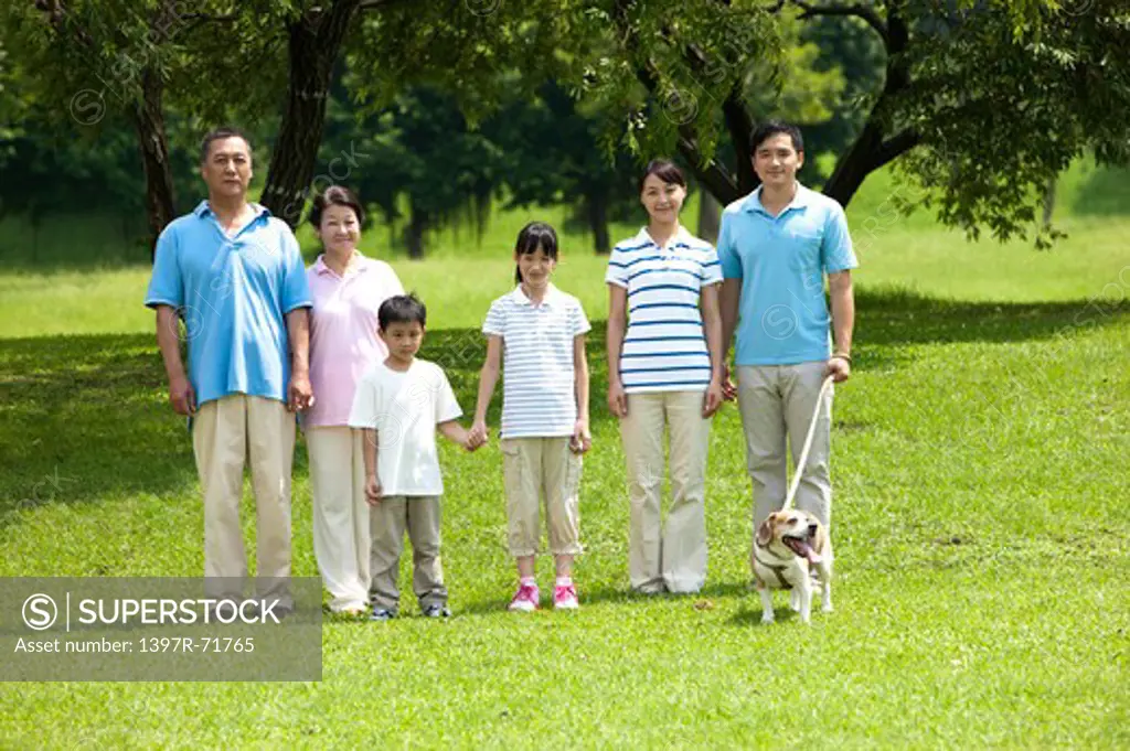 Multi-generational family standing side by side in a park with their pet
