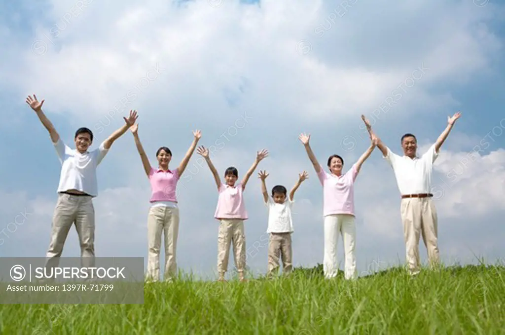 Multi-generational family standing in a row on lawn with their arms up and outstretched