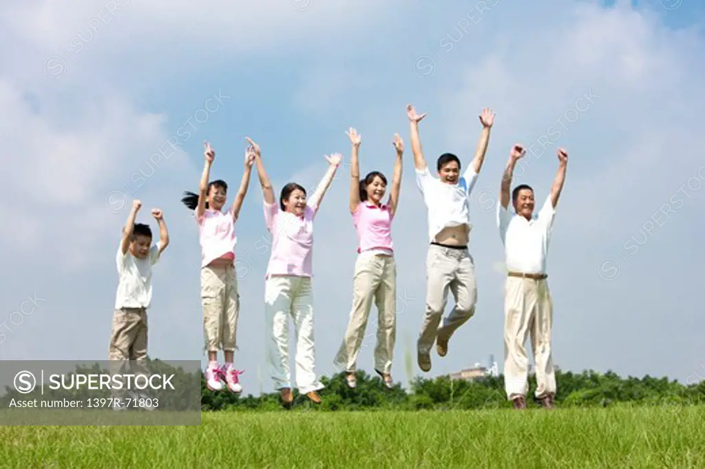 Multi-generational family jumping in mid air in a row on lawn, arms up