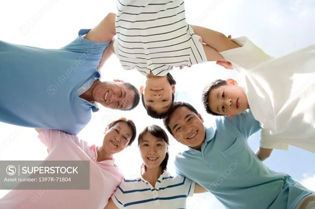 Multi-generational family standing in a huddle arm in arm, smiling, low angle view