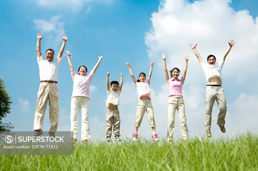 Multi-generational family jumping in a row on lawn, arms up