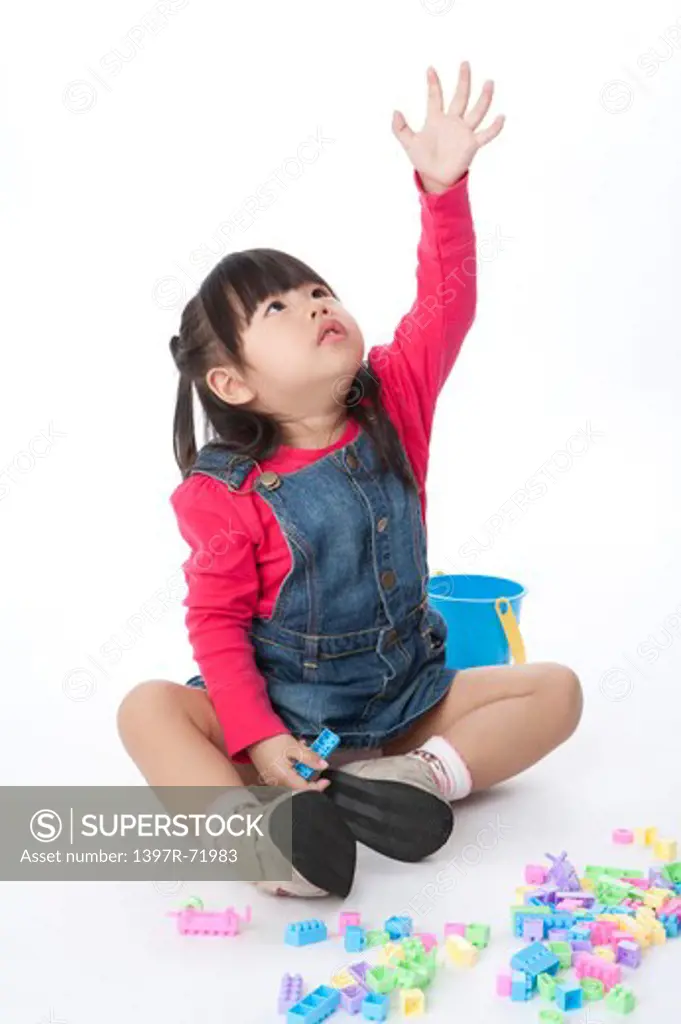 Little girl sitting on floor with toys and lifting her arm