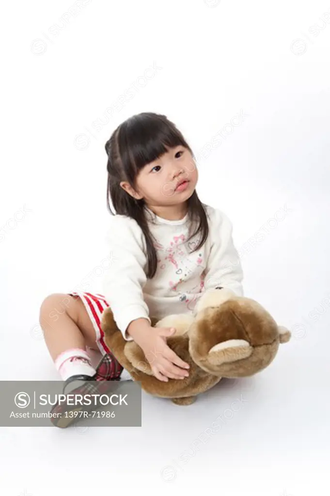 Little girl sitting on floor and holding teddy bear