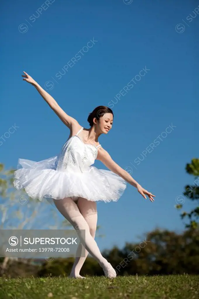 Ballet dancer dancing on the lawn and looking down with smile