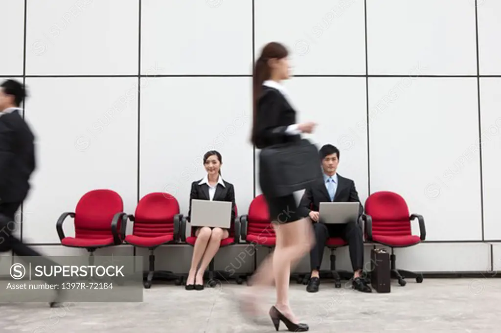 Business people walking in a hurry with others sitting in the background working with laptop