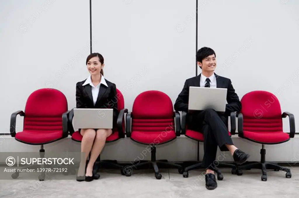 Business people sitting in office chairs working with laptops