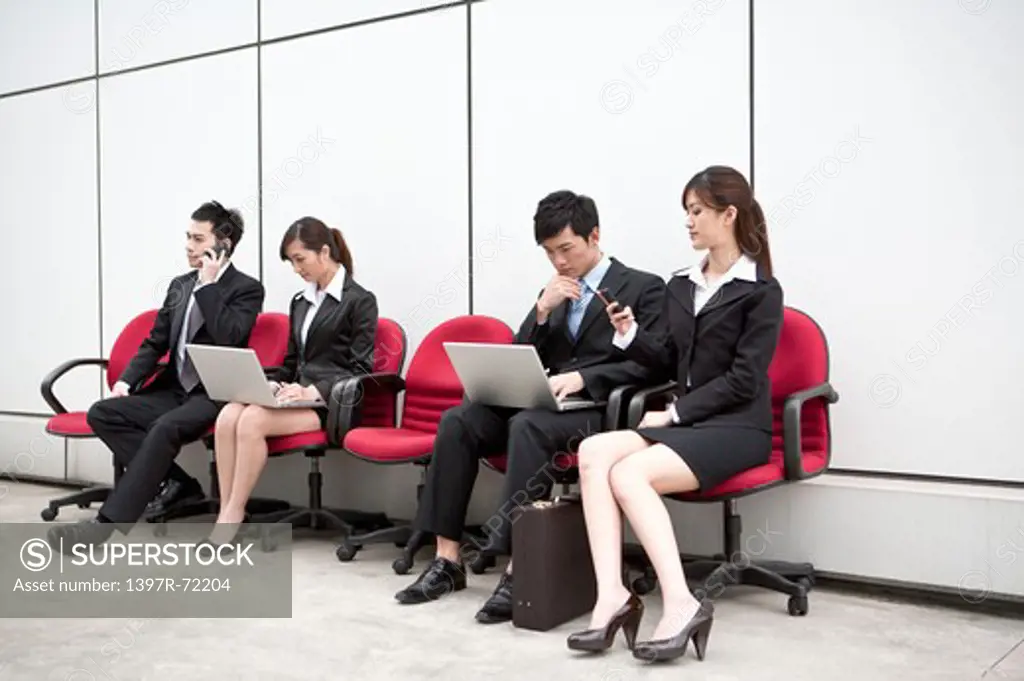 Business people sitting in office chairs in a row busy with their work