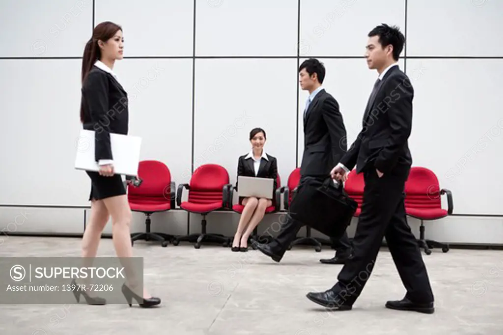 Business people walking in a hurry with one sitting in the background working with laptop