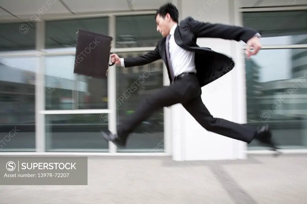 Businessman running and leaping in mid air, blurred motion