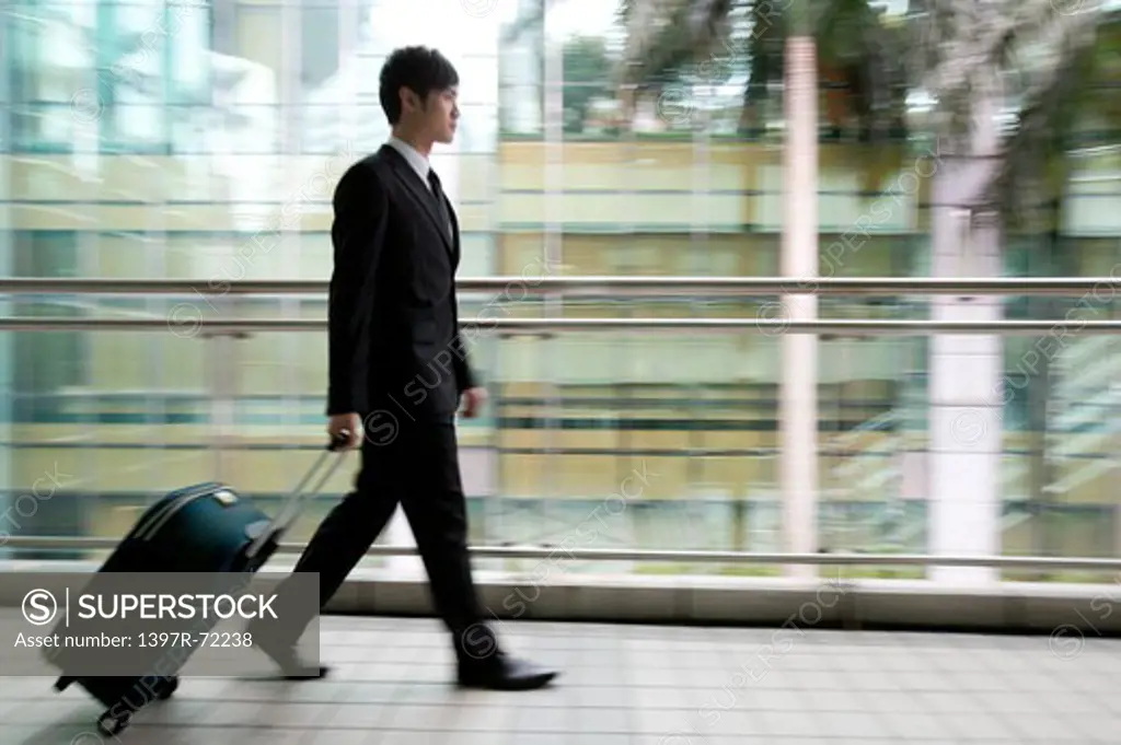 Businessman walking with rolling suitcase, blurred motion