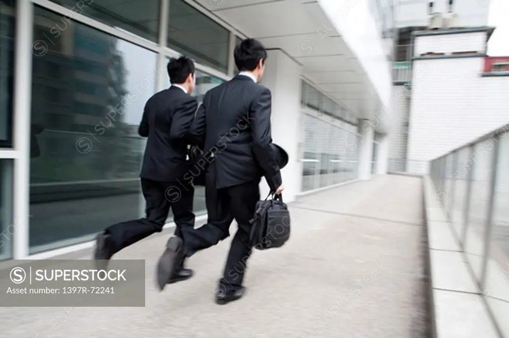 Businessmen running side by side, blurred motion, rear view