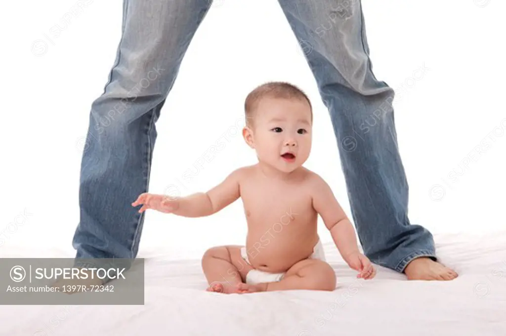 Baby girl sitting on bed with father standing behind