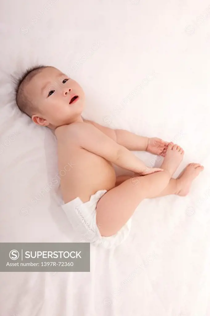 Baby girl lying on side, holding feet, directly above