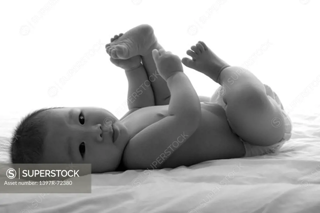 Baby girl lying on back holding foot