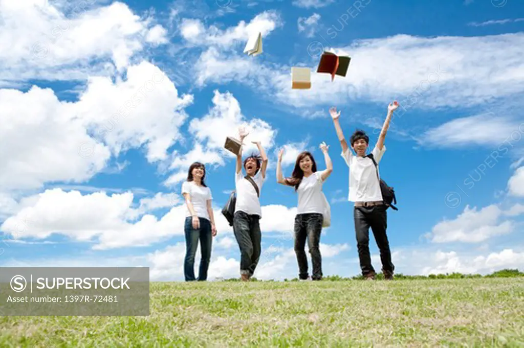Young adults standing on the lawn with books in mid-air