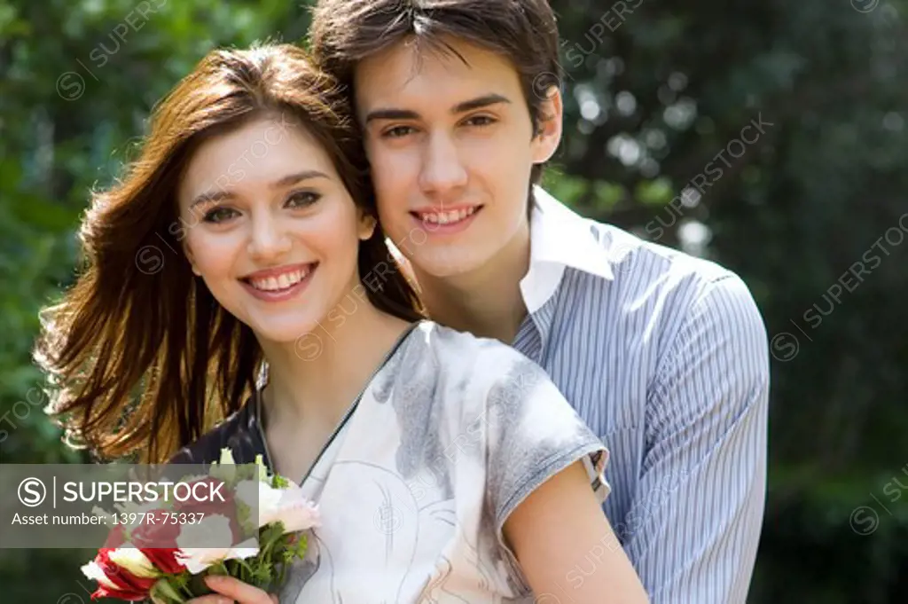 Portrait of embracing young couple, woman holding flowers