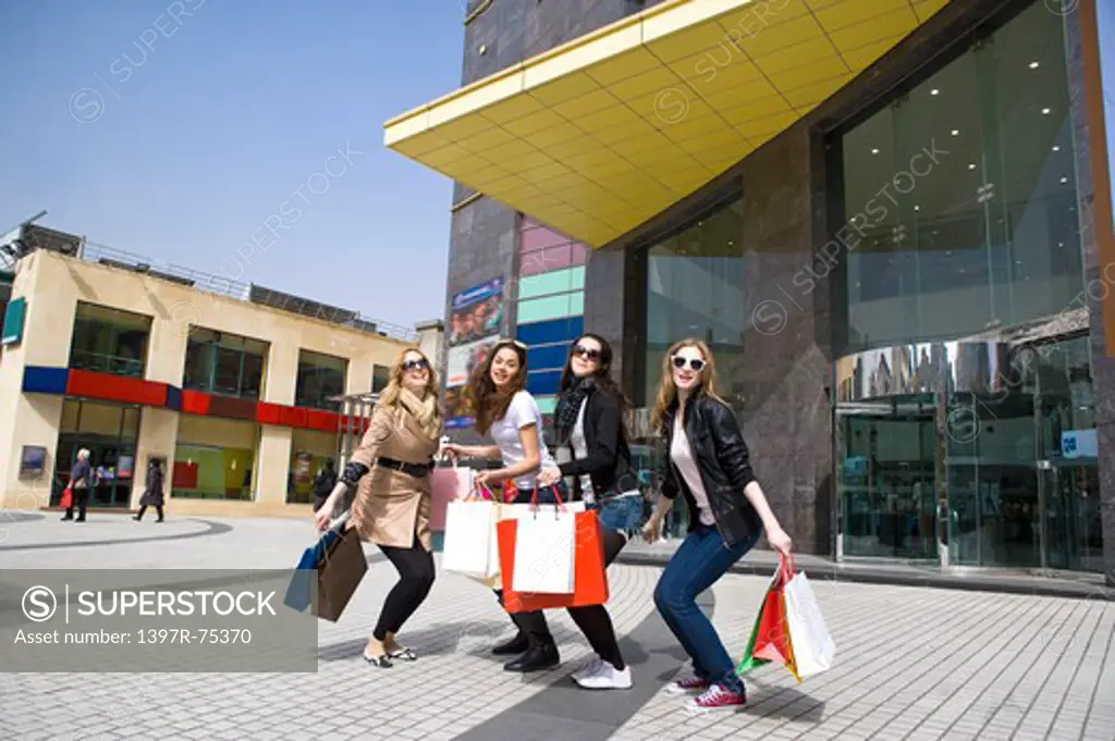Four young women jumping together and holding shopping bags, Shopping