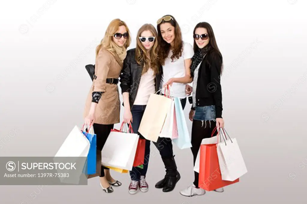 Four young women standing together with shopping bags and smiling at the camera, Shopping