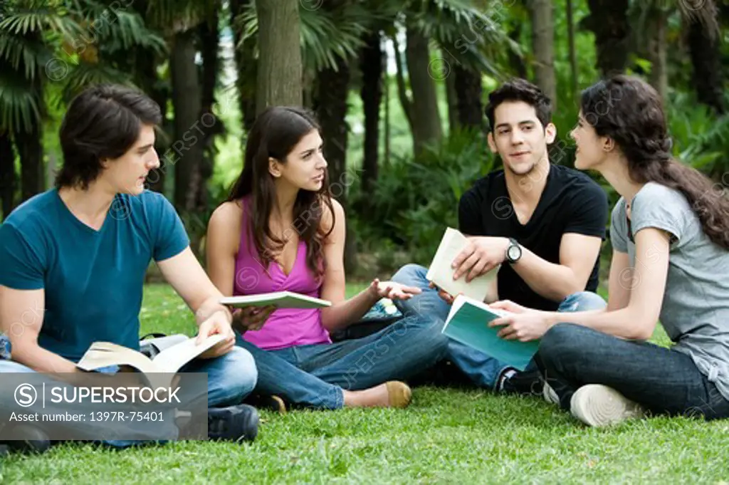 Four young friends sitting on lawn, reading books