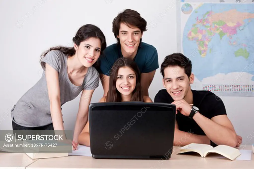 Four students in classroom with books and laptop