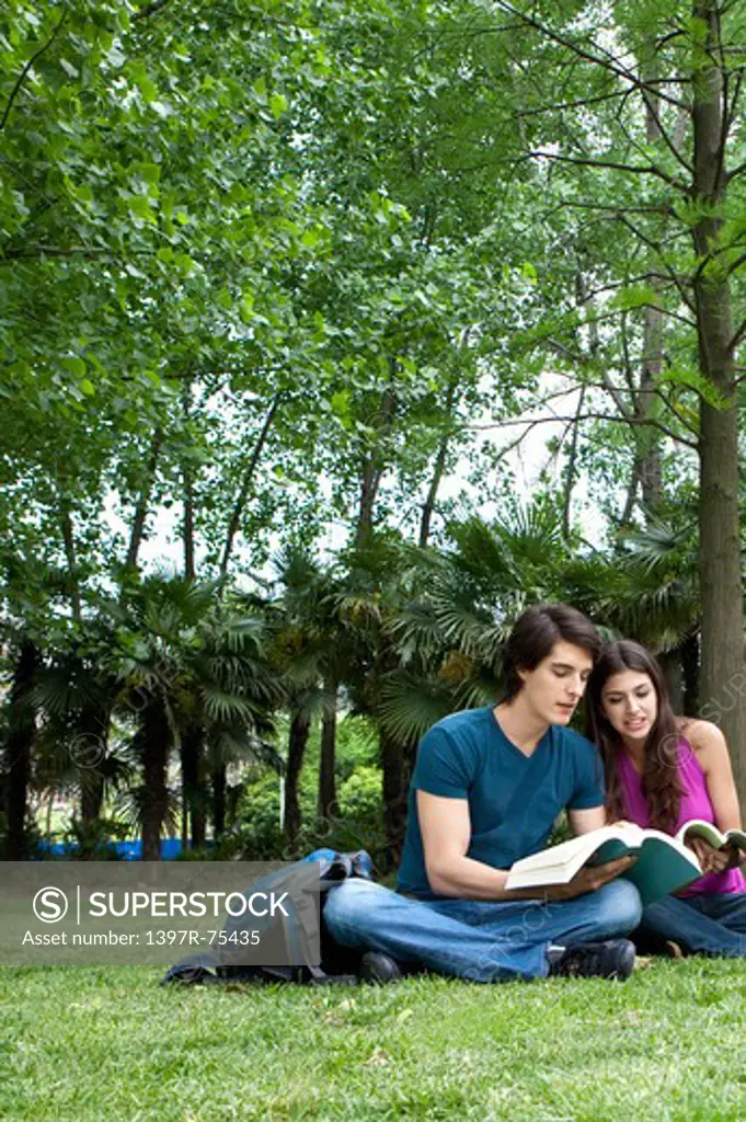 Young couple sitting on lawn, reading books