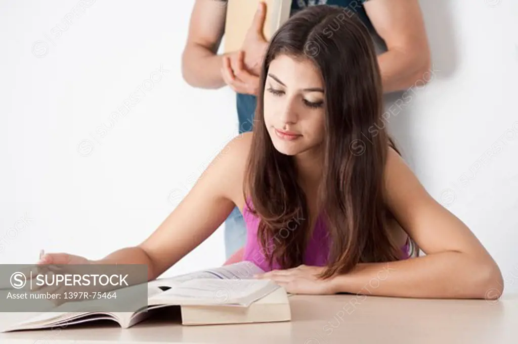 Young woman sitting at a desk studying with friend standing behind
