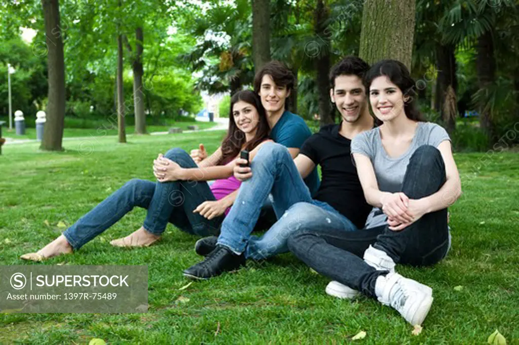 Four young friends sitting on lawn by a tree, smiling