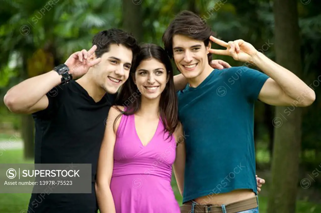 Three young friends standing arm in arm smiling, giving peace sign