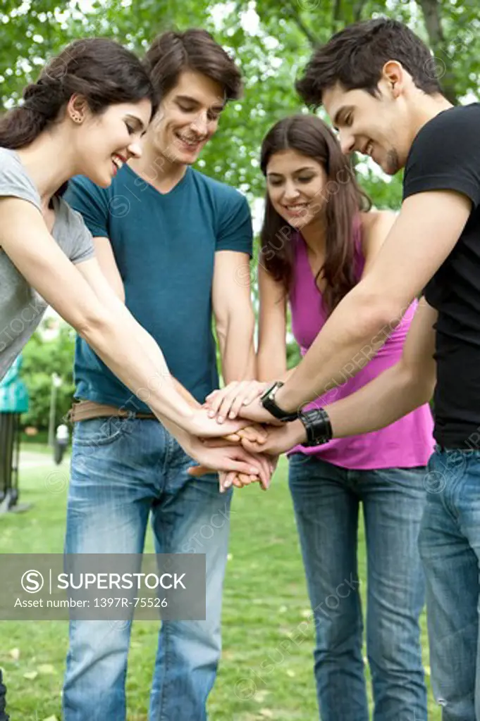 Four young friends overlapping hands in a park