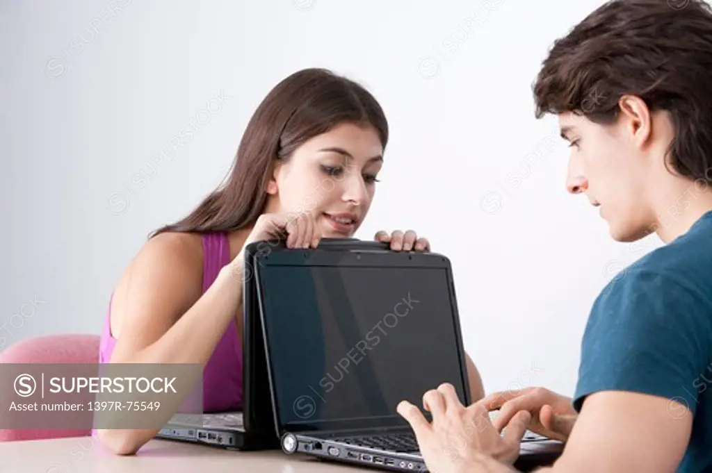 Two young friends using laptops face to face, woman looking over
