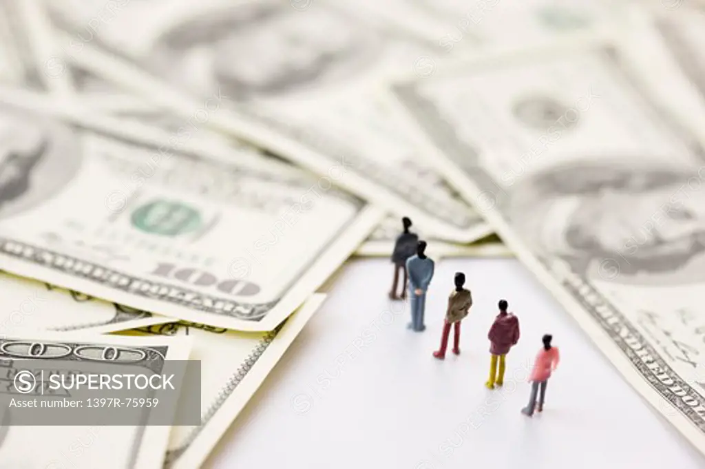 Figurine forming a line walking to stacks of US Paper Currency