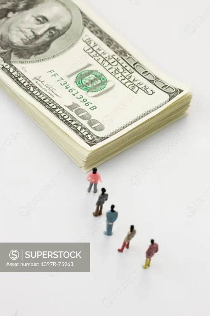 Figurines waiting in line before a stack of US hundred dollar bills