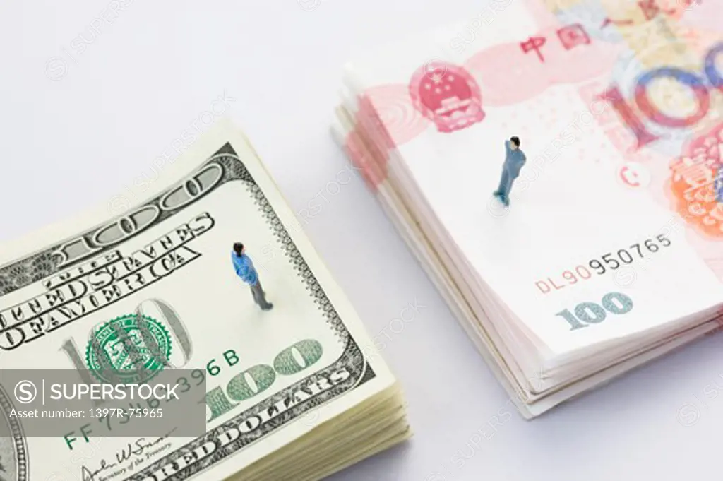 Two figurines on top of stacks of Chinese and US Paper Currency separately