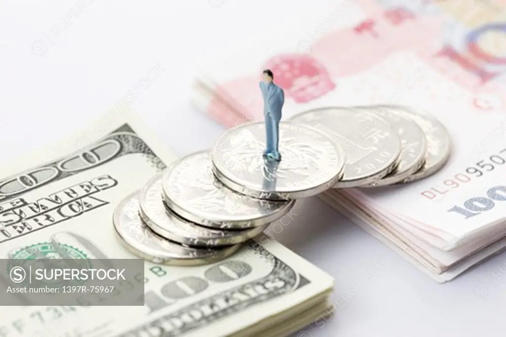 A figurine standing on a bridge made of coins across two stacks of Paper Currency, one side of US Dollars and the other side China Currency