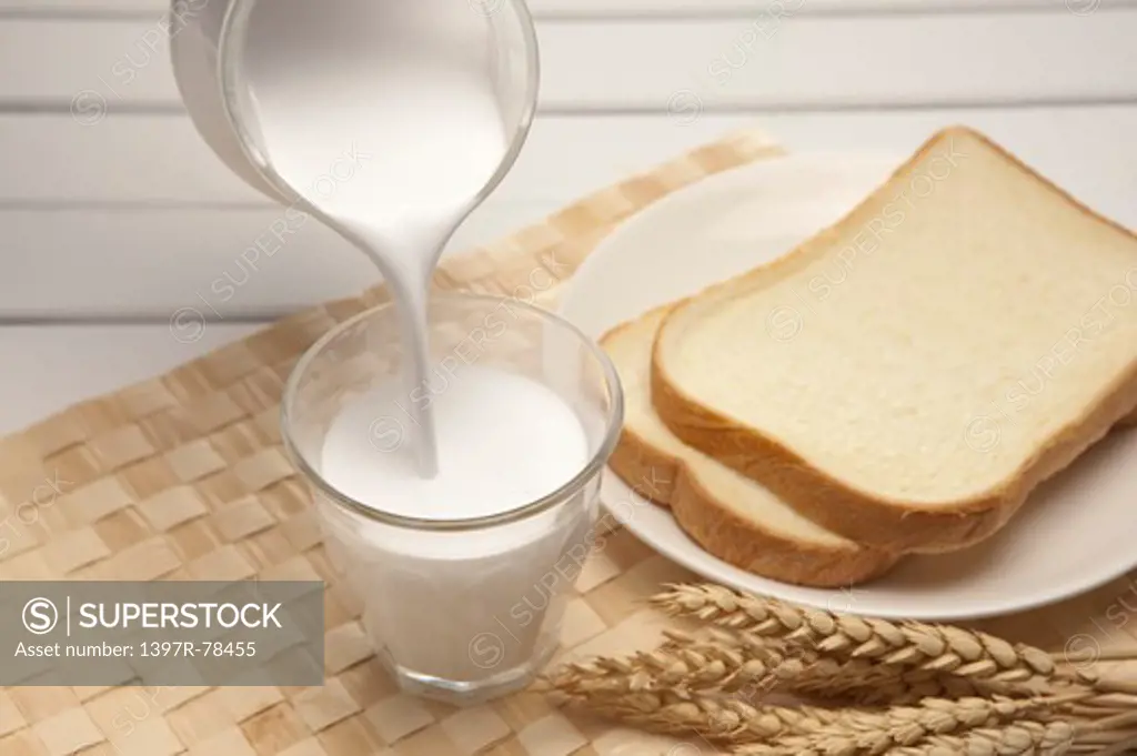 Poured milk in glass and sliced loaf of bread on plate