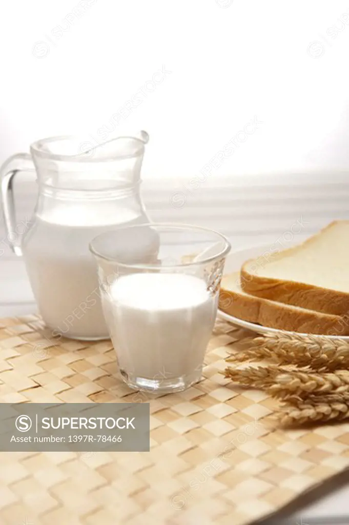 A pitcher and a glass of milk and loaf of bread