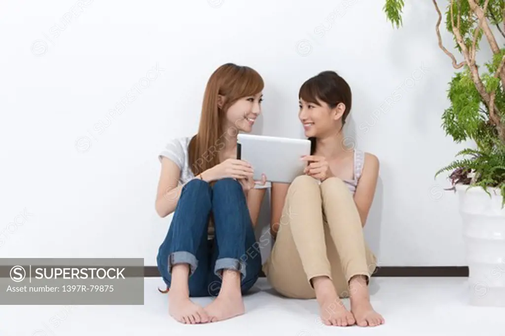 Young women sitting on the floor and playing with digital tablet together