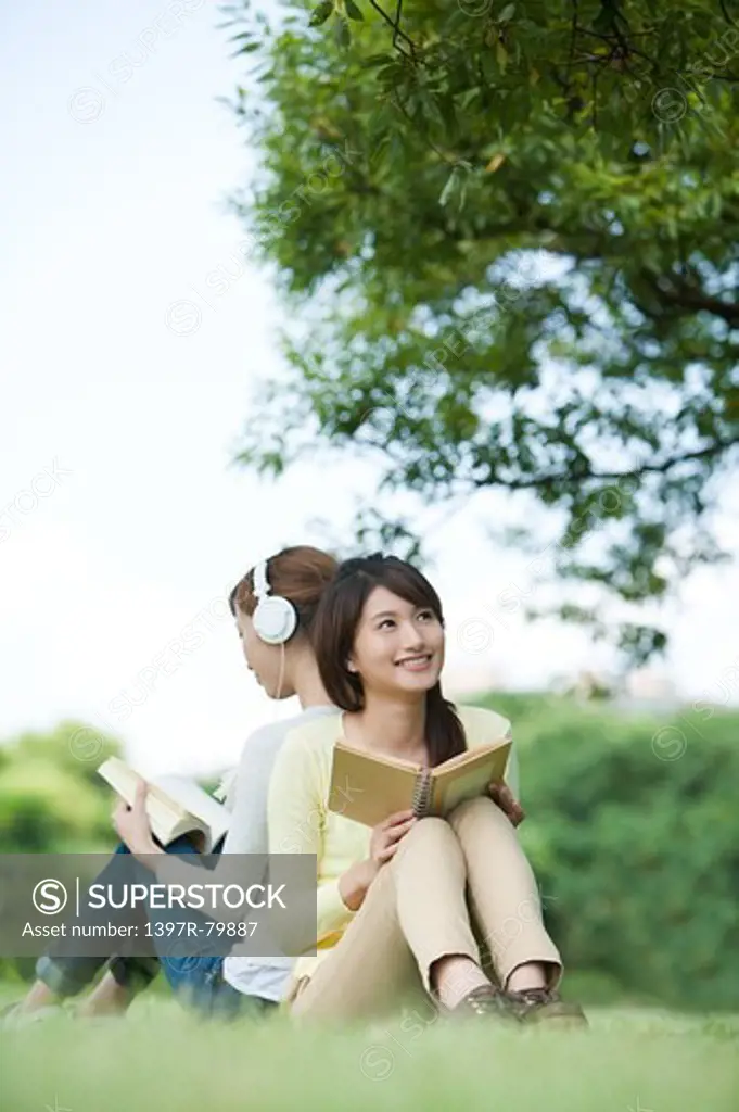 Young women sitting on the lawn and holding books with smile