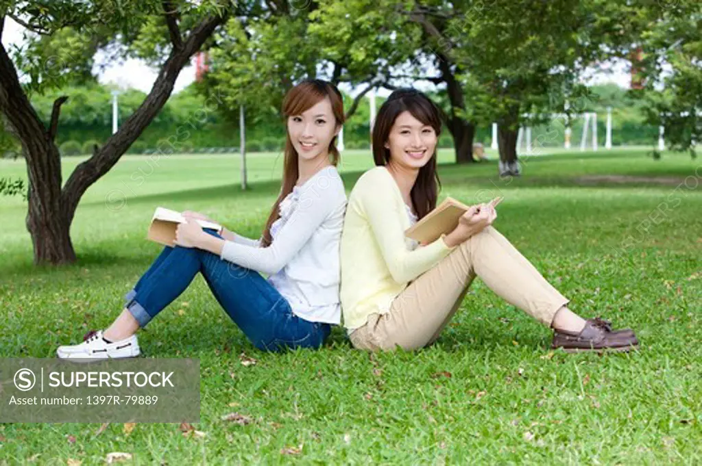 Young women sitting on the lawn and holding a book with smile