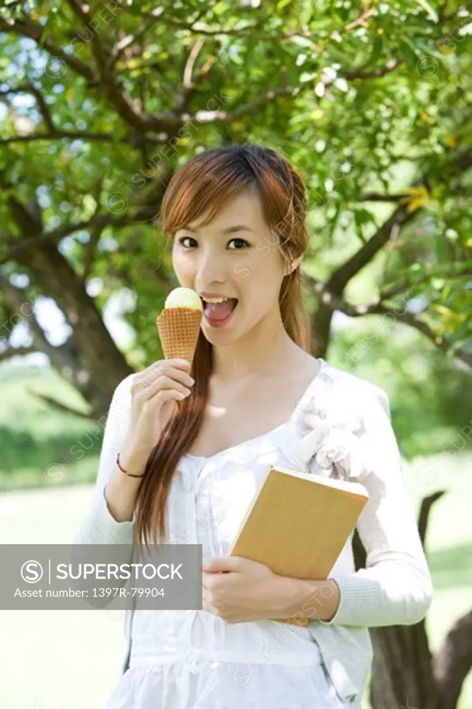 Young woman holding ice cream and book with smile