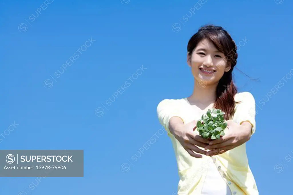 Young woman holding potted plant and smiling at the camera