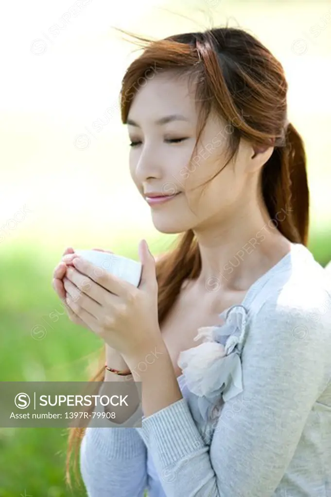 Young woman holding a cup and smiling with eyes closed